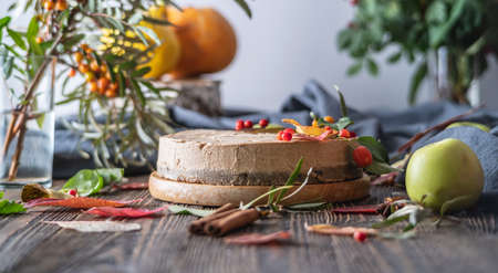 Brown mousse cake decorated with autumn leaves and berries. Wooden background. Concept of autumn mood and atmosphere.の写真素材
