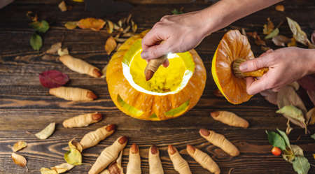 Hand is putting the cookie in the form of a finger inside the pumpkin with the face cut out. Concept of celebrating Halloween and the sinister atmosphere.の写真素材