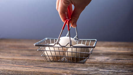 Hand is holding a small basket with fresh organic eggs. Concept of online purchasing of farm...
