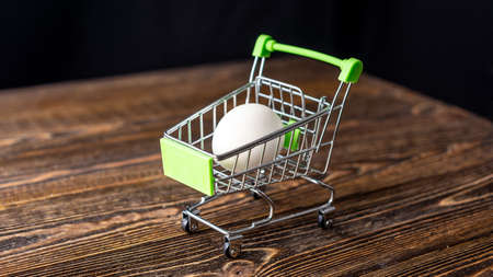 White raw fresh eco egg in a shopping cart on a wooden background. Concept of online purchasing of farm products delivery.の写真素材