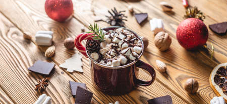 A cup of aromatic tasty hot chocolate with marshmallows decorated with red candy on a wooden table surrounded by Christmas accessories. Concept of a festive atmosphere and cozy New Year mood.の写真素材