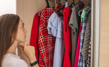 A young woman is choosing a dress in her wardrobe. Concept of choosing an outfit for a holiday or everyday life at home.の写真素材