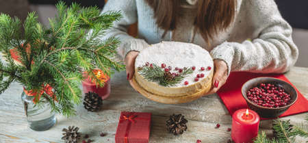 Woman is holding a festive white mousse cake covered with coconut flakes imitating snow and...