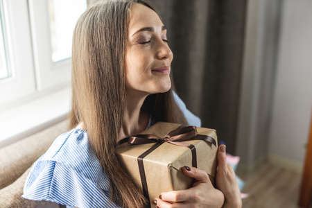 Happy cute young woman with a gift box in her hands at home. Concept of a holiday, dreamy and cozy...