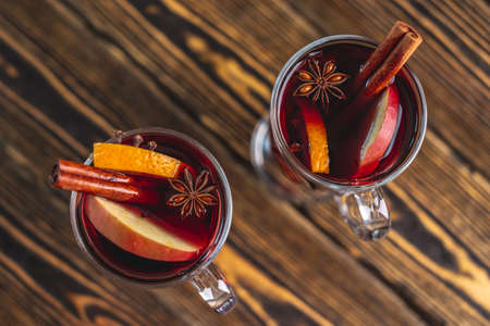 Couple glass cups with mulled wine decorated with cinnamon, star anise and fruit on a wooden table....