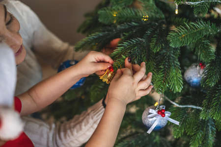 Mother and her child son are holding a Christmas tree ball toy to hang on a branch. The concept of a...