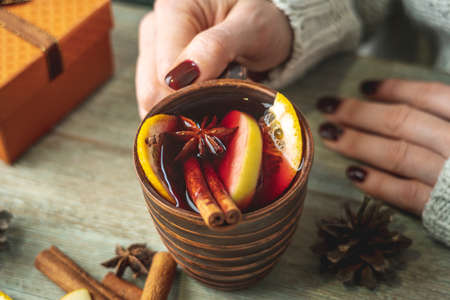 Woman's hands in a warm sweater are holding a cup of aromatic hot mulled wine on a wooden table. Concept of a festive atmosphere and cozy winter mood.の写真素材