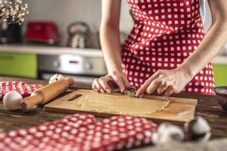 Woman making delicious homemade cookies in the shape of Christmas tree in her kitchen. Concept of fresh homemade cakes and cozy festive atmosphere.の写真素材