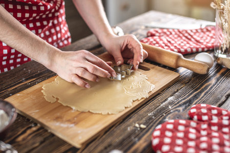 Woman making delicious homemade cookies in the shape of Christmas tree in her kitchen. Concept of...