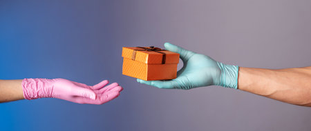 A man's hand in a blue glove is giving a gift box to a woman's hand in pink glove on a blue and gray...