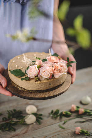 Woman is holding in her hands a beautiful raw mousse cake decorated with tenderness flowers. Concept...