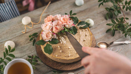 Woman's hand is cutting a beautiful raw mousse cake decorated with tenderness flowers. Concept of a romantic atmosphere and spring mood.の写真素材