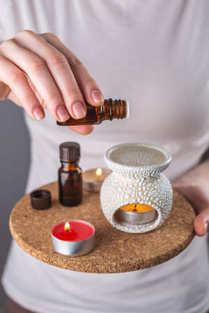 A woman is dripping organic essential oil into an aroma lamp for a relaxing and pleasant aromatherapy procedure. Closeup.の写真素材