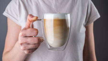 Woman is holding a fresh, aromatic latte coffee, poured in layers into a transparent double glass cup. Closeup.の写真素材