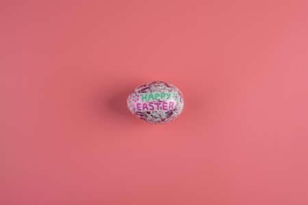 One shiny fashionable egg with Happy Easter inscription on a pink background. Copy space and top view.の写真素材