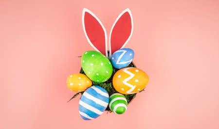 Bright Easter colorful eggs, paper rabbit ears on a pink background. Top view.