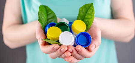 Hands are holding a handful of colorful plastic lids with green leaves. Concept of environmental...