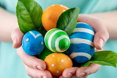 Woman is holding colorful eggs and green leaves in her hands. Concept of Easter and springtime. Closeup.の写真素材