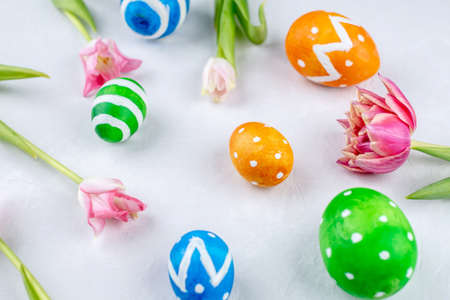 Cute colorful Easter eggs painted with paints and spring flowers tulips on a white background.