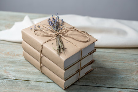 A stack books wrapped of craft paper, neatly tied with rope and decorated with lavender flowers on a blue wooden tableの写真素材