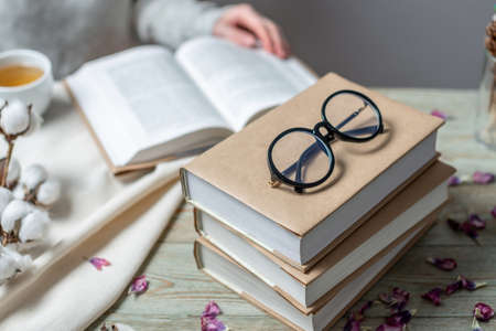 Stack of books with craft paper covers on a wooden table. In the background, a woman is reading a book. Concept of reading and choosing a book.の写真素材