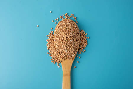Green buckwheat in a wooden spoon on a blue background. Concept of proper nutrition and healthy food.の写真素材