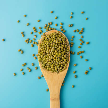 A portion of dry Asian beans in a wooden spoon on a blue background. Concept of proper nutrition and healthy food.の写真素材