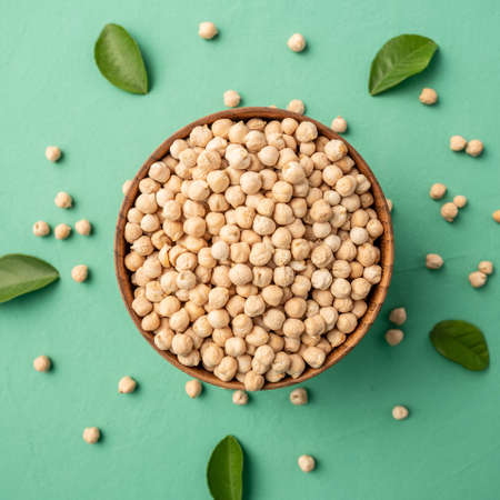 Wooden bowl with raw dried chickpeas and leaves on a green background. Concept of a balanced diet and healthy food. Top view.の写真素材