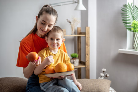 Young mom and a little child in bright clothes are sitting with a plate of oranges and lemons in their hands. Concept of healthy family, fruit and vitamin consumption, family lifestyle and pastime.の写真素材