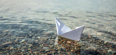 White paper boat in the clear water of large lake with a stony bottom.の写真素材