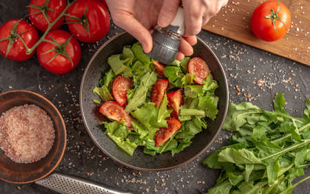 Women's hands are sprinkling a light vitamin vegetable salad with spices. Concept of cooking healthy...