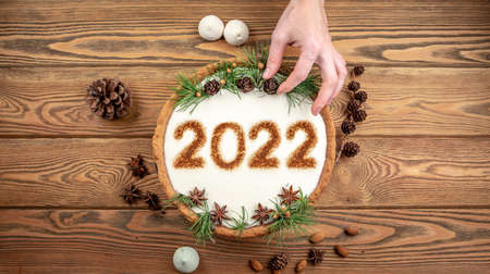 Hand is decorating a festival cake with cones, coniferous branches and star anise. Concept of the New Year 2022.の写真素材