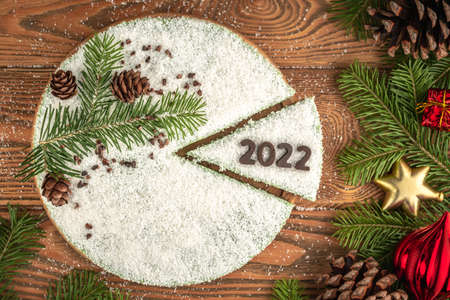 White festive mousse cake covered with coconut flakes, imitating snow. On the piece of cake, the number 2022 is put out with chocolate. Concept of a New year.の写真素材