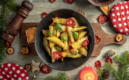 On a brown cutting board is a plate with the tasty appetizing dish. Around on a wooden background are green coniferous branches, festive accessories. Concept of New Year and Christmas, top viewの写真素材