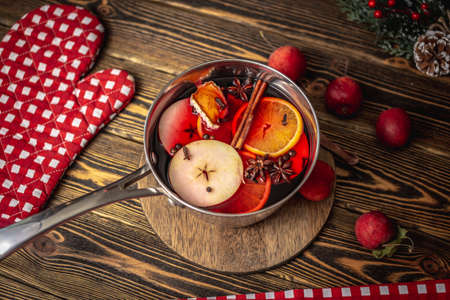 Saucepan with fragrant spicy hot mulled wine on a wooden table surrounded by festive accessories and fruits. Concept of a cozy holiday atmosphere, New Year and Christmas mood.の写真素材