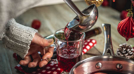 Woman is pouring fragrant hot punch into a clear mug. Concept of a cozy festive atmosphere, New Year...