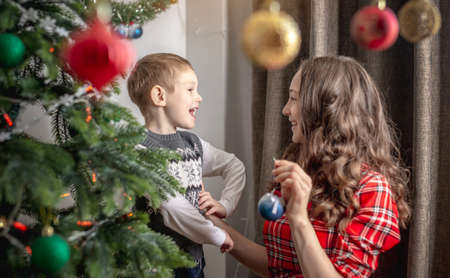 Mom with her child is decorating together the Christmas tree with toys and balls. Concept of family...