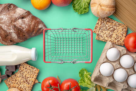 Set of fresh products and a miniature shopping basket on a green background top view. Online shopping concept, food delivery.の写真素材