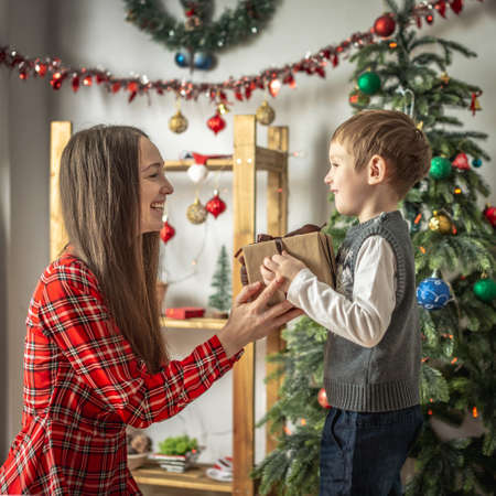 Happy mom and child near the Christmas tree are giving gifts and smiling. Concept of New Year mood, festive atmosphere.の写真素材
