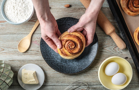 Female hands carefully shifting the fresh warm cinnamon rolls from the baking tray to the plate. Concept of delicious homemade pastries and a cozy atmosphere. top view.の写真素材