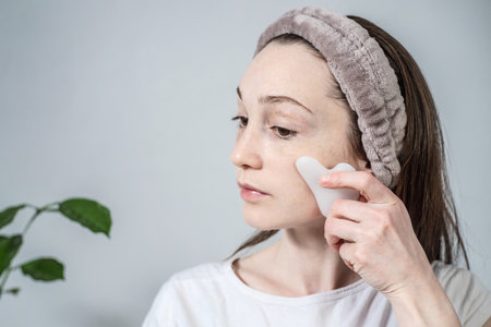 Woman is doing a massage with a gouache scraper massager with oil. Concept of facial care, morning rituals.の写真素材