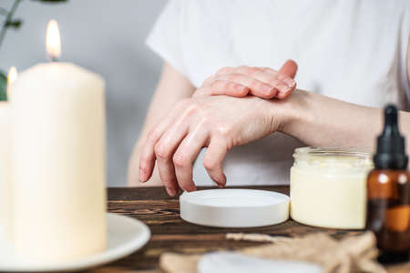 Woman is smearing her hands with a natural organic cream doing a massage. Aroma lamp with essential oils and candles on the table. Concept of skin and self care, atmosphere of harmony and relaxationの写真素材