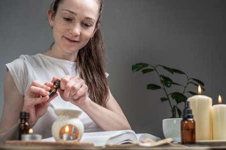 Book on the table, burning candles and a woman is pouring essential oil into an aroma lamp. Concept...