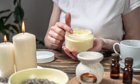 Woman is smearing her hands with a natural organic cream doing a massage. Aroma lamp with essential oils and candles on the table. Concept of skin and self care, atmosphere of harmony and relaxationの写真素材