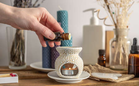 Female hand is holding a bottle of essential oil and dripping it in an aroma lamp for aromatherapy...