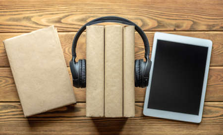 A stack of books with headphones on and tablets on wooden background. The concept of modern technological education and the study of books.の写真素材