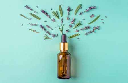 Bottle of cosmetic oil with leaves and flowers on a blue-green background. Concept of lavender fragrance, essential oil for beauty and healthy procedures. Top view and flat lay.の写真素材