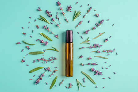 Glass bottle with cosmetic oil and leaves and flowers on a blue-green background. Concept of...