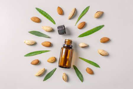 Bottle of cosmetic oil and nuts and leaves of almond on a gray background. Concept of organic skin care and natural almonds fragrance. Top view and flat layの写真素材