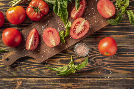 On the wooden table there is a cutting board, ripe homemade tomatoes and fragrant green basil. top view.の写真素材